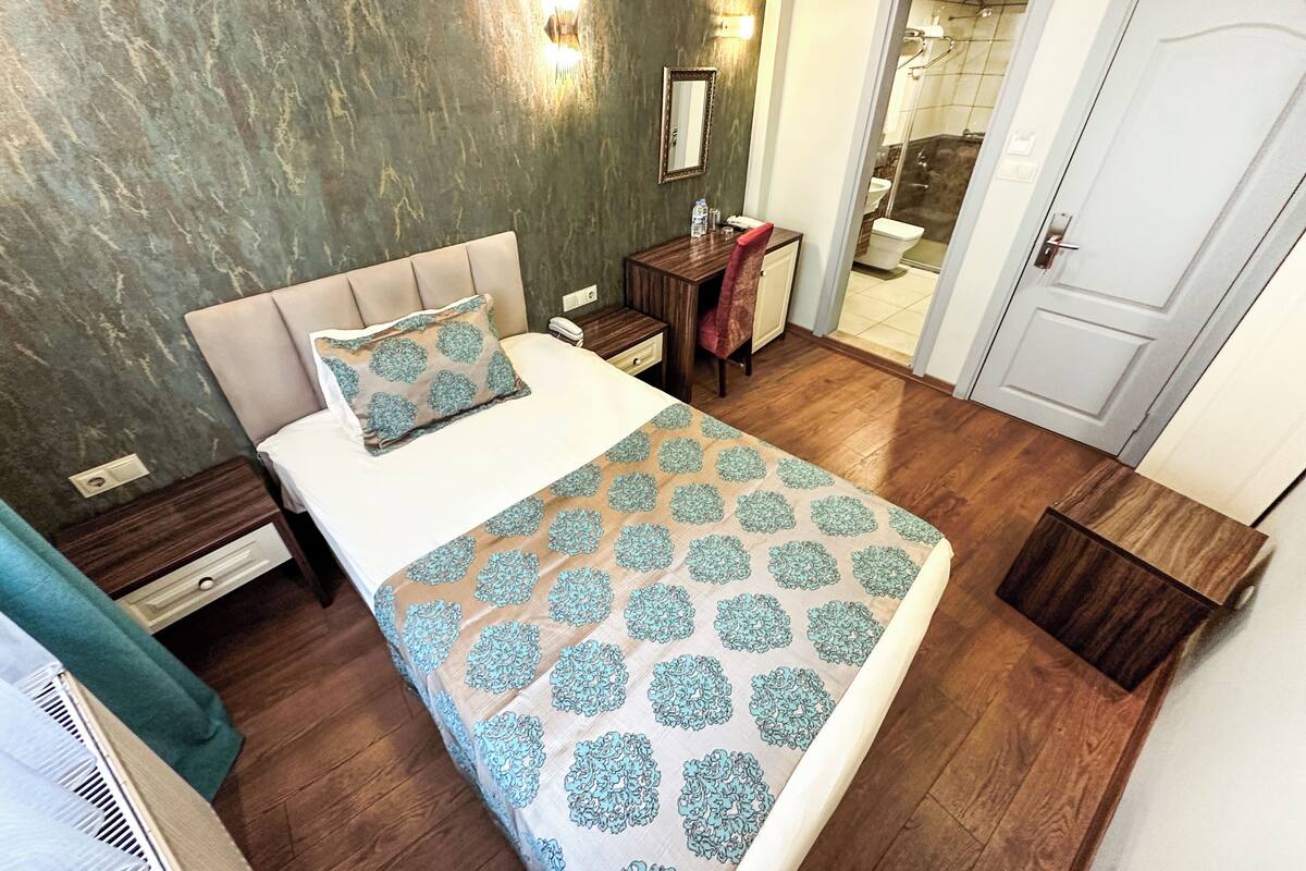 A bedroom with a bed, a nightstand, a dresser, a mirror, and a bathroom visible through an open door.