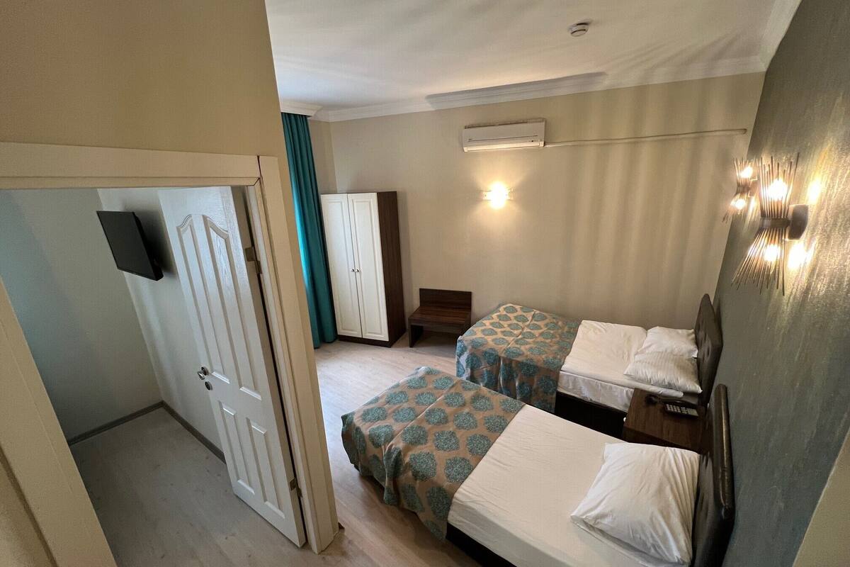 A hotel room with two single beds, a wardrobe, a desk, and a television.