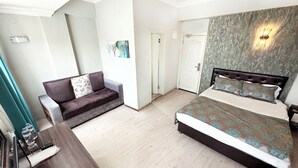 Quarto com cama, sofá, escrivaninha e luminária na parede.