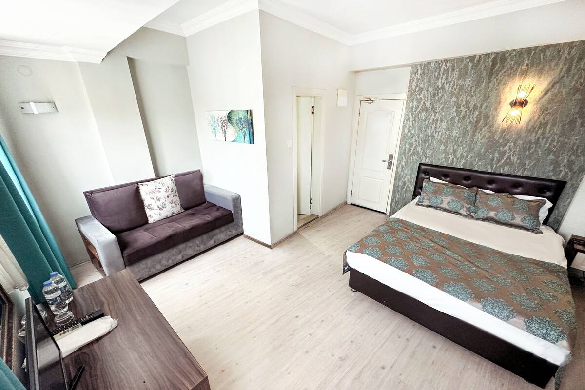 A bedroom with a bed, a sofa, a desk, and a wall-mounted light fixture.