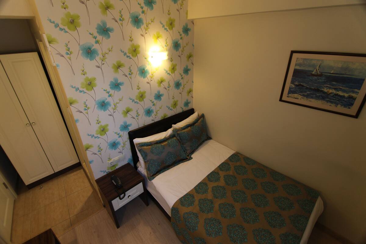A bedroom with a bed, nightstand, and a wall with floral wallpaper.