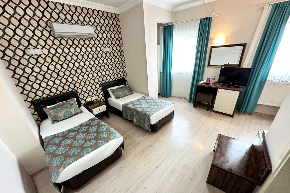 A hotel room with two beds, a desk, a television, and a window with curtains.