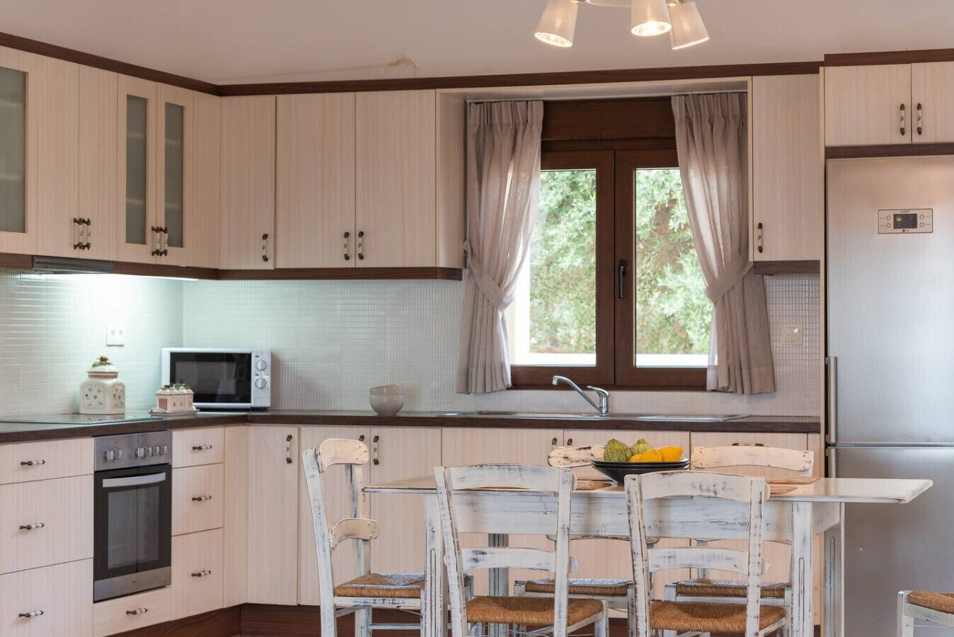 Una cocina con armarios de tonos claros, microondas, estufa, lavaplatos y una mesa de comedor con sillas.