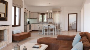 A spacious living area with a fireplace, a dining table with chairs, and a kitchen in the background.