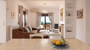 A living room with a brown sofa, a dining table with a bowl of fruit, a TV, and a fireplace.