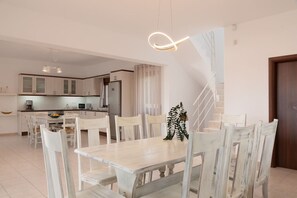 A modern kitchen with white cabinets, a dining table with chairs, and a staircase.
