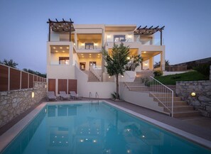 Una casa moderna de dos pisos con piscina, mobiliario exterior y una escalera que conduce al piso superior.