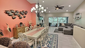 Uma sala de jantar com uma mesa e cadeiras brancas, um lustre e arte decorativa nas paredes.