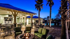 An outdoor patio area with a fire pit, green seating, and a pool in the background. - ☀️2 Masters~2 Golf Carts Included~6 Bikes~Pools~Last Call at NatureWalk 30A (Santa Rosa Beach)