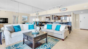 A spacious living room with two white sofas, a dark coffee table, and a kitchen area in the background. - Gulf Views~Beachfront Pool~Walk2Beach~2BR East Pass 209 (Destin)