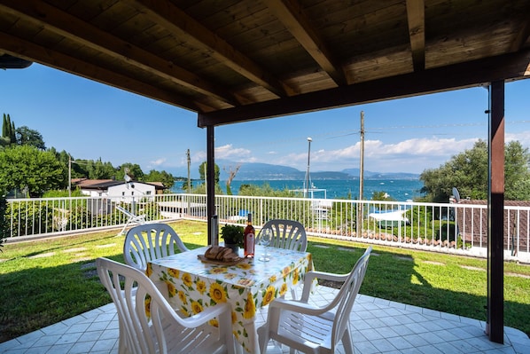 An outdoor patio with a table set for two, overlooking a scenic view of the sea and mountains.