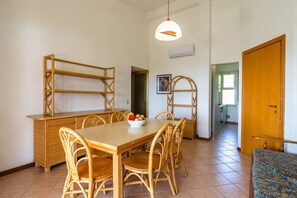 A dining area with a wooden table and chairs, a fruit bowl, and a hanging light fixture.