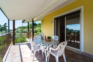 A balcony with a table and chairs, a glass door, and a view of greenery and hills.