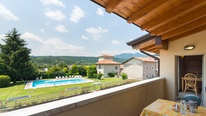 A balcony with a view of a swimming pool, a dining table, and a chair. - Apartment in Salò with Pool & Olive Groves (Cunettone)