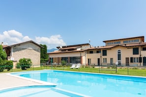 Una piscina con lettini, un edificio con tetto in tegole e cielo sereno.