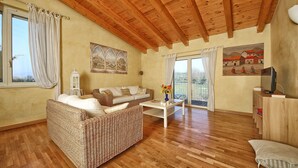 A living room with a wicker sofa, a white coffee table, wooden flooring, a wooden ceiling, a TV stand, and a painting on the wall. - Modern Salo Flat with Pool (Cunettone)