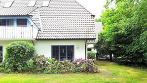 Une maison à deux étages, avec un toit en tuiles, un petit jardin agrémenté de plantes fleuries et une pelouse bien entretenue.