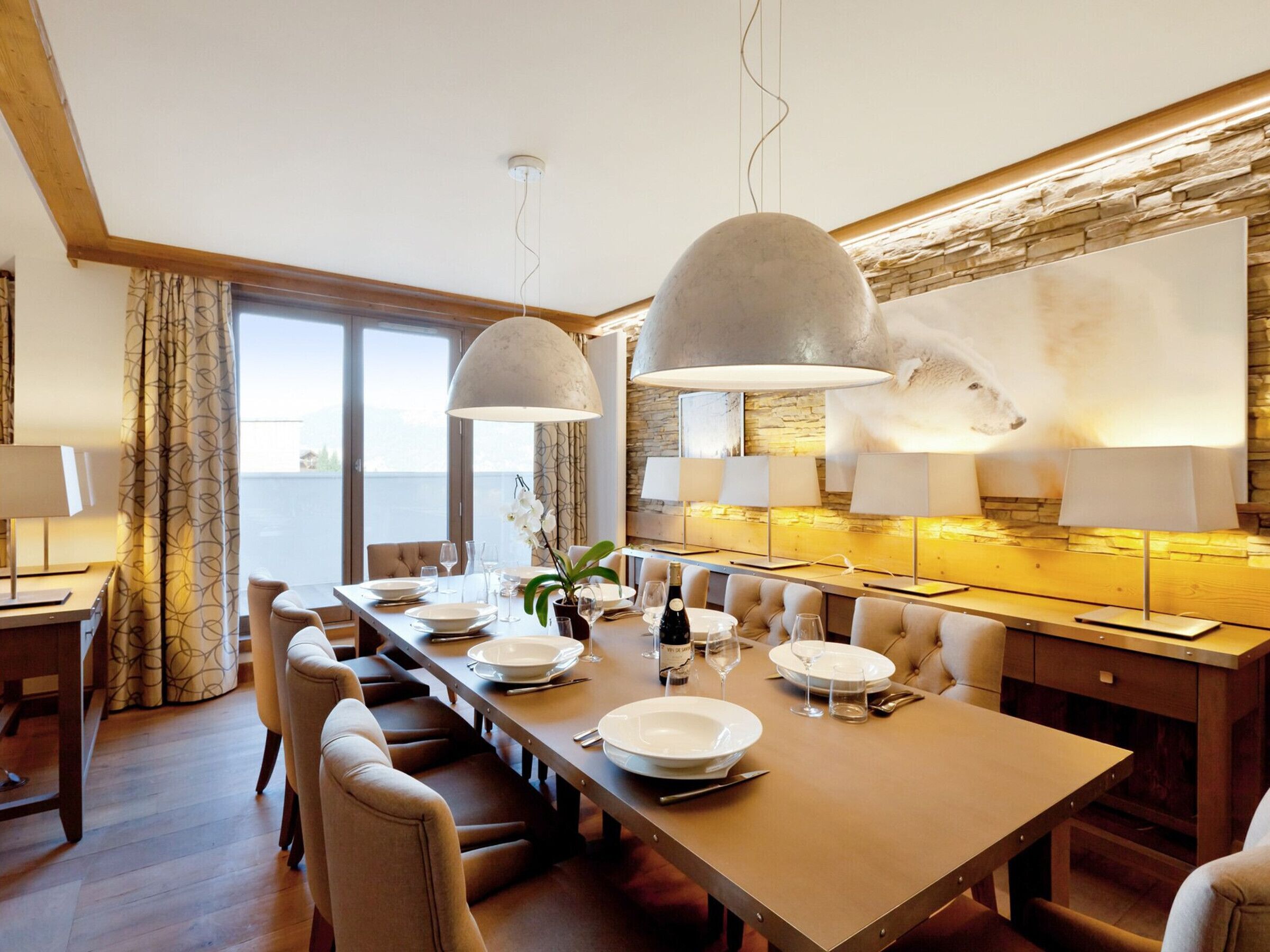 A dining area with a long table, multiple chairs, and pendant lighting.