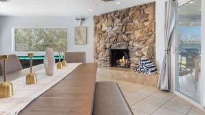 A modern living room with a stone fireplace, a pool table, and a large window overlooking a deck. - Hot Tub, Pool, Firepit, Bball, Foosball, Hammocks (Yucca Valley)
