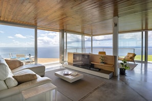 Amplia sala de estar con un ventanal con vistas al mar, un sofá moderno, una mesa de centro y un mueble para televisión.