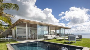 A modern house with a pool, outdoor seating, and a view of the sea.