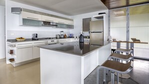 A modern kitchen with white cabinetry, a central island, bar stools, and a large window with blinds.