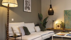 Een moderne zithoek met een witte bank, een houten vloerlamp, een hangende hanglamp en een kleine tafel met boeken en een vaas.