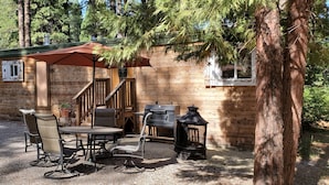 A wooden cabin with a covered patio, outdoor seating, a grill, and a lantern.