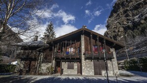 Un edificio in pietra con un balcone in legno, facciata in pietra e montagne sullo sfondo.