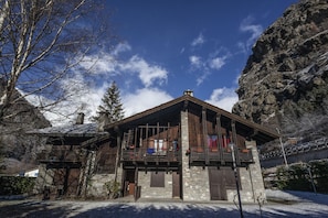 Ein Steinhaus mit einem hölzernen Balkon, einer Steinfassade und einer Bergkulisse.