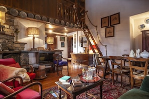 Ein gemütliches Wohnzimmer mit Kamin, Holzmöbeln und einer Treppe, die in einen oberen Bereich führt.