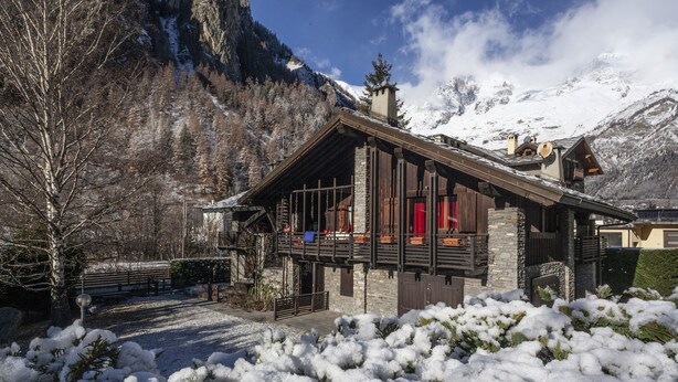 Un chalet con un balcone, pareti in pietra e vista sulle montagne innevate.