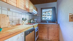 Een compacte keuken met houten kastjes, een vaatwasser en een raam met uitzicht op een bergpanorama.