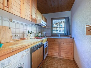 A compact kitchen with wooden cabinets, a dishwasher, and a window overlooking a mountain view. - Family Apartment in Val-d'Isère - 5 People - WIFI (Val-d'Isère)