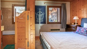 Een houten slaapkamer met een bed, een raam, een houten deur en een badkamer.