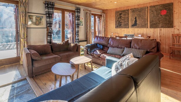 Een gezellig blokhut interieur met houten wanden en plafond, een bruine leren bank, een blauwe fauteuil en een kleine ronde tafel.