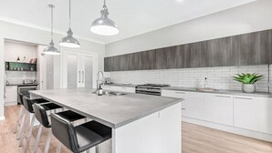 Een moderne keuken met een centraal eiland, roestvrijstalen apparatuur en hangende lampen.