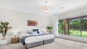 Een moderne slaapkamer met een groot raam, een bed met een blauwe plaid en een schilderij aan de muur.