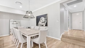Een moderne eetruimte met een houten tafel, witte stoelen met bekleding en een hanglamp.