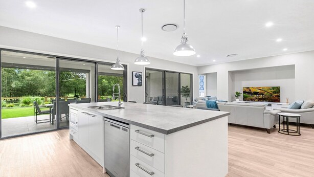 Een moderne keuken met een groot schiereiland, roestvrijstalen apparatuur en een schuifdeur naar een tuin.