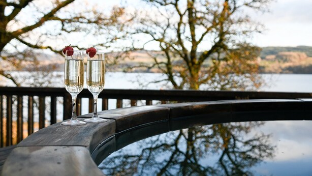 Two glasses of champagne with strawberries on a wooden railing by a lake.