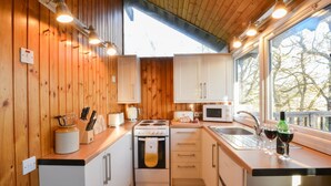 A compact kitchen with wooden walls, white cabinets, a stove, a microwave, and a sink.