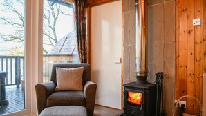 A cozy room with a stone fireplace, a comfortable armchair, and a view of the outdoors through a large window.