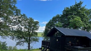 A rustic cabin by a lake with a wooden deck and a metal roof.