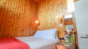 A wooden-paneled room with a bed, bedside lamps, a mirror, and a vase with flowers.