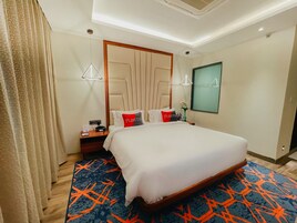 A hotel room with a large bed, a nightstand, a lamp, and a mirror.