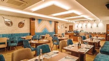 Un restaurante con mesas y cabinas, una cocina al fondo y espejos decorativos en la pared.