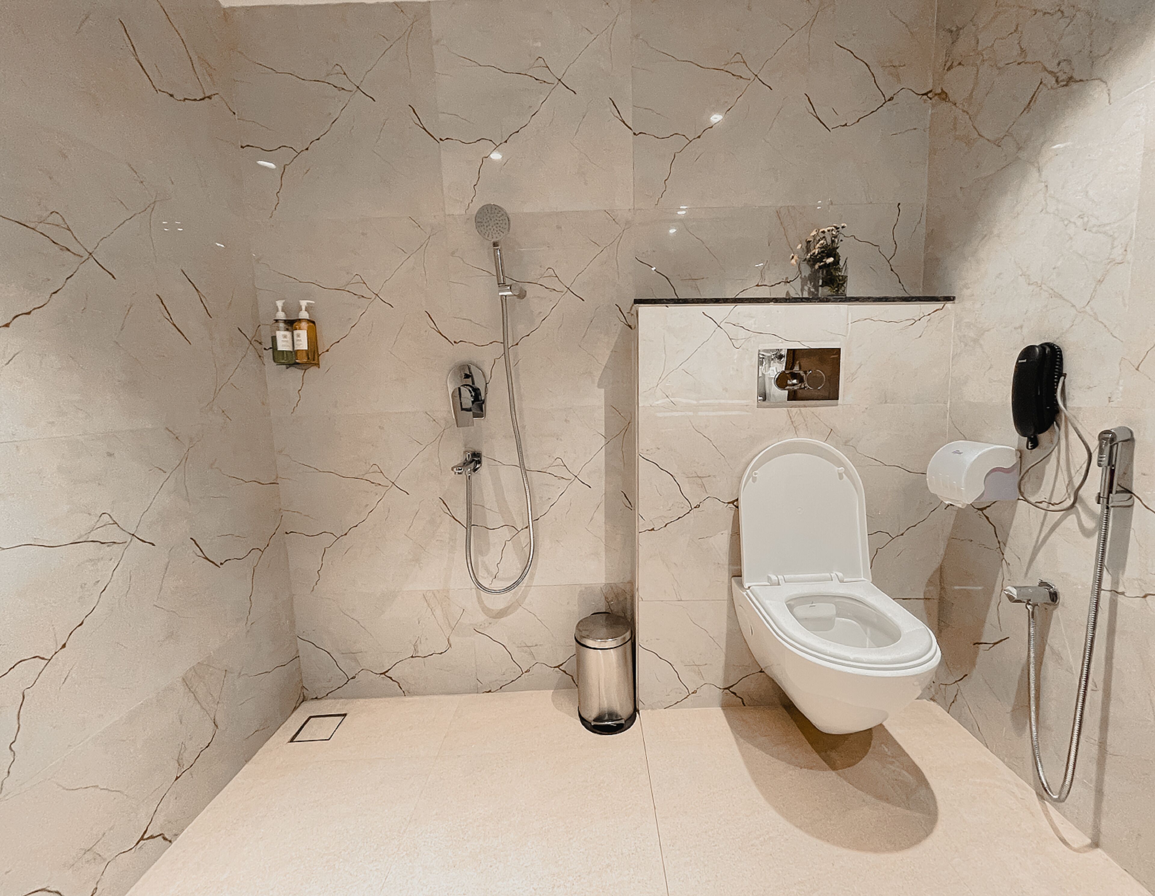 A modern bathroom with a marble floor, a toilet, a shower, and a small trash bin.