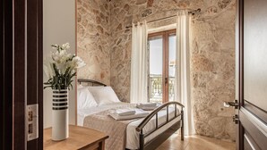 Ein Schlafzimmer mit Steinwand, einem Bett mit weißer Bettwäsche, einem hölzernen Nachttisch und einer Vase mit Blumen.