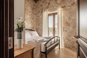 A bedroom with a stone wall, a bed with white linens, a wooden nightstand, and a vase with flowers.